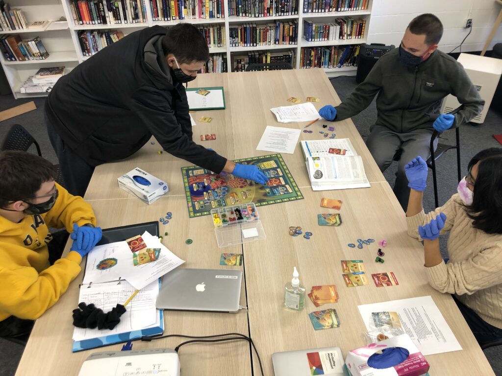 Students gathered around a gameboard at a large table